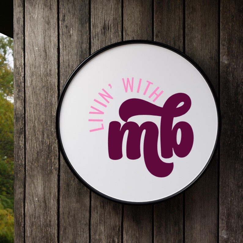 May include: Round white sign with the words "Livin' With mb" in pink and dark purple lettering. The sign has a black border and is mounted on a weathered wooden surface.