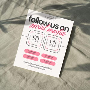 Könnte beinhalten: Ein weißer Flyer mit dem Text "follow us on social media" in Schwarz und Pink. Er enthält zwei QR-Code-Felder und pinkfarbene Social-Media-Buttons. Der Flyer ermutigt zum Scannen des QR-Codes mit einem Smartphone.