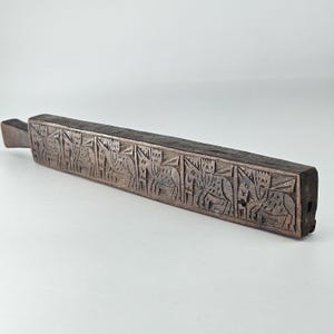 May include: A dark brown, rectangular wooden carving with a handle. The carving features a series of stylized animal figures. The wood has a weathered appearance, suggesting age and use. The piece is likely a decorative or functional item.