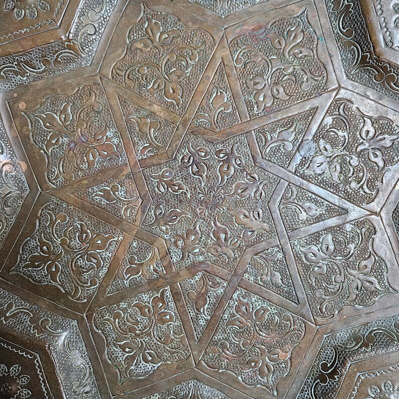 May include: A metallic copper-toned tray featuring an intricate embossed pattern of a large central star surrounded by geometric shapes. Each section is filled with detailed floral motifs and textured backgrounds, creating a relief effect across the surface.
