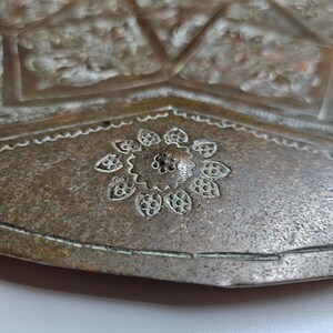 May include: A metallic tray with a weathered bronze-toned finish featuring intricate hand-engraved floral patterns and geometric borders. The surface displays a central flower motif surrounded by detailed etched lines and textured metalwork.