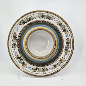 May include: A ceramic serving bowl with a central dip bowl. The bowl features a white rim with acorn and leaf designs, a green, yellow, and blue striped center, and a brown border. The bowl is supported by a clear stand.