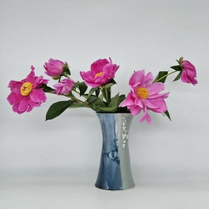 May include: A bouquet of pink peonies with yellow centers arranged in a blue and white ceramic vase.