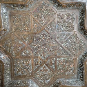 May include: A square copper tray featuring an intricate, embossed eight-pointed star design at its center. The surface is decorated with detailed floral motifs and textured patterns, showcasing a warm, metallic brown finish throughout.