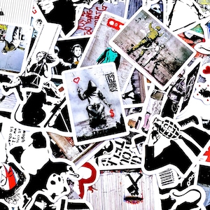 Può includere: Una collezione di vari adesivi con grafica e illustrazioni in bianco e nero. Alcuni adesivi presentano opere d'arte in stile Banksy, tra cui una figura che tiene in mano un palloncino a forma di cuore e un soldato. Altri adesivi hanno testo e altri disegni.