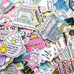 May include: A collection of colorful stickers with positive affirmations and cute illustrations. Designs include a jar of sprinkles, a toaster with "MONDAY", a perfume bottle, and a coffee cup. Text includes "Kindness", "Remember", and "I am amazing".