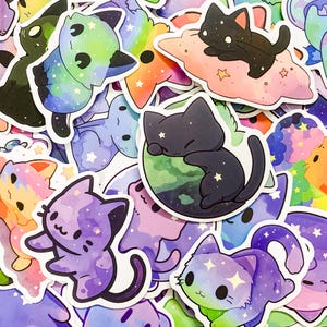 May include: A collection of colorful cat stickers with galaxy and star designs. The stickers feature various poses and expressions, including a cat sleeping on a planet, a cat on a cloud, and a cat with a rainbow tail.
