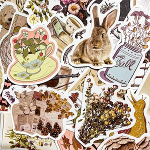 May include: A collection of vintage-style stickers featuring a teacup with strawberries, a brown rabbit, a mason jar with flowers, a bouquet of dried flowers, and a snail. The stickers are printed on white paper with a glossy finish.