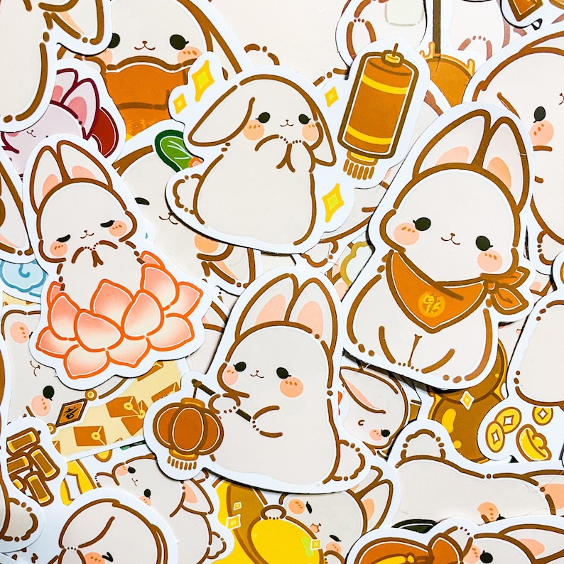 May include: A collection of white bunny stickers with various designs, including a bunny holding a lantern, a bunny sitting on a lotus flower, and a bunny with a red scarf. The stickers are on a white background.
