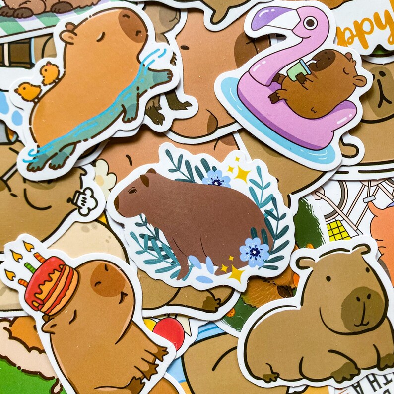 May include: A collection of colorful capybara stickers. Some stickers feature capybaras with birthday cakes, swimming, or relaxing on a flamingo float. Other stickers show capybaras surrounded by flowers or simply sitting.