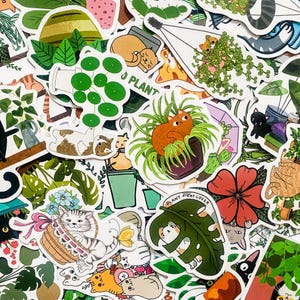 May include: A collection of colourful stickers featuring cats, plants, and the text "Plant + Cat Lover". The stickers are on a white background and have a variety of designs, including cats in pots, cats with plants, and cats with flowers.