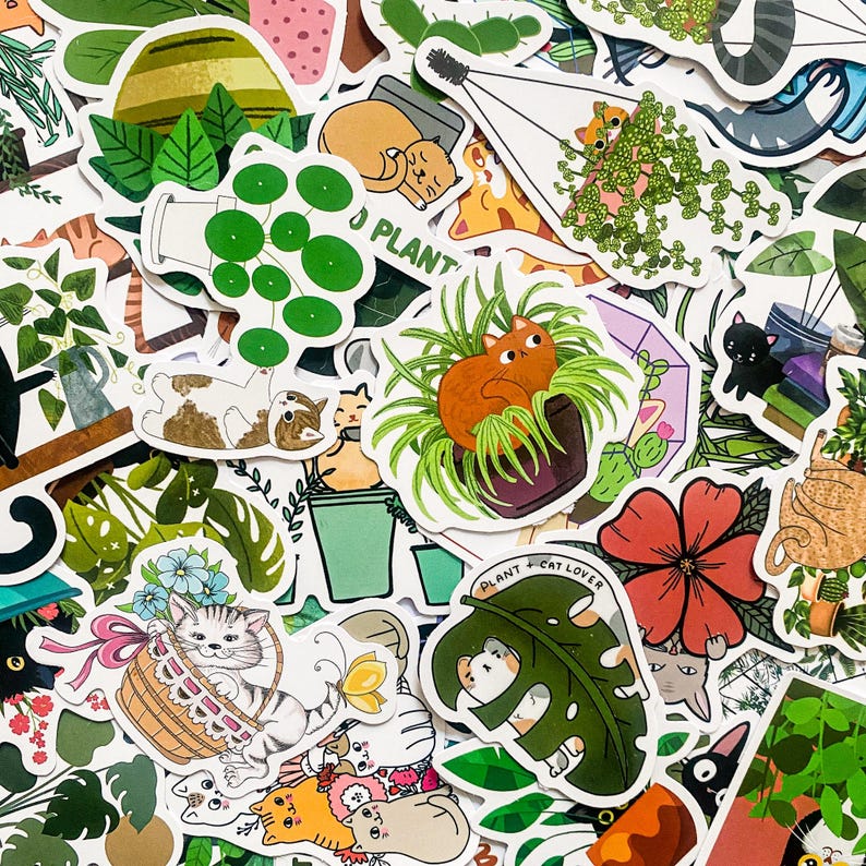 May include: A collection of colourful stickers featuring cats, plants, and the text "Plant + Cat Lover". The stickers are on a white background and have a variety of designs, including cats in pots, cats with plants, and cats with flowers.