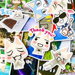 May include: A collection of colorful stickers featuring cartoon cats with different expressions. The stickers are printed on white paper and have a glossy finish. Some of the stickers have text, including "Thank you!" and "Zzzzzz".