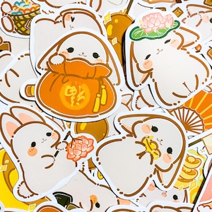 May include: A collection of stickers featuring cute cartoon bunnies in various poses. The bunnies are holding items like a red bag with Chinese characters, a lotus flower, and a gold coin. The stickers are on a white background.
