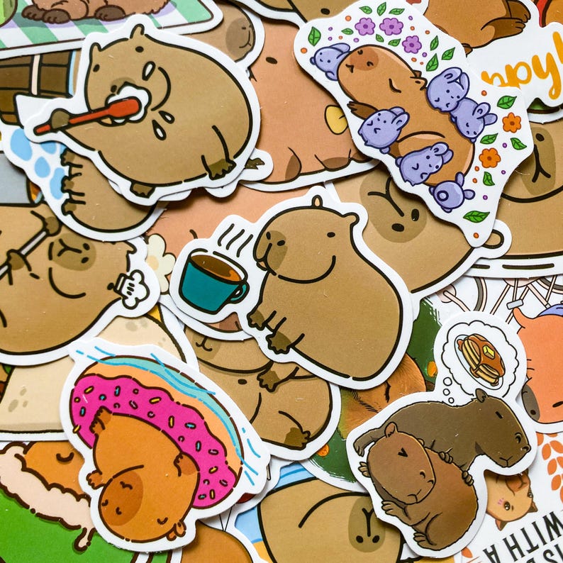 May include: A collection of whimsical stickers featuring cartoon capybaras in various poses. Some stickers show capybaras with a toothbrush, a cup of coffee, and a donut. The stickers are in shades of brown, pink, and blue.