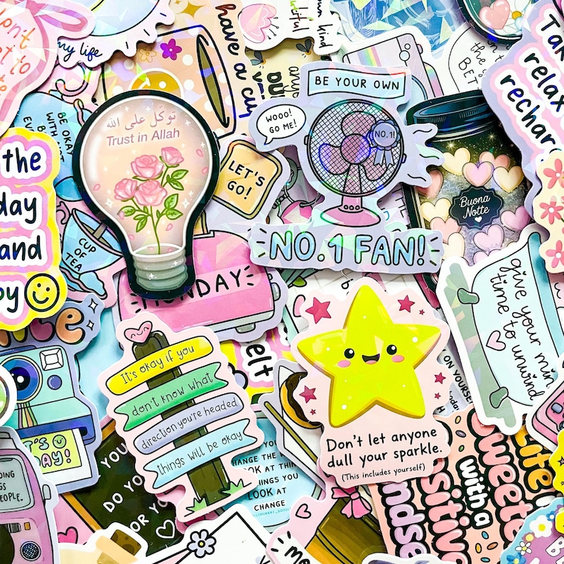 May include: A collection of colorful stickers with various designs and text. Stickers include a lightbulb with roses, a fan with "No. 1 Fan!", a yellow star, and phrases like "Be Your Own" and "Don't let anyone dull your sparkle."