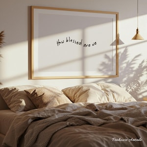 Könnte beinhalten: Ein gerahmter Druck mit dem handgeschriebenen Text „How blessed are we“ hängt über einem Bett mit beiger Bettwäsche. Der Raum wird von natürlichem Licht beleuchtet, das Schatten auf die Wand und das Bett wirft. Der Rahmen ist aus hellem Holz.