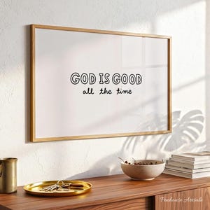 Puede incluir: Una impresión enmarcada con las palabras "GOD IS GOOD all the time" en letras negras. El marco es de color marrón claro y la impresión se muestra sobre un fondo blanco. La impresión está colgada en una pared blanca encima de un mueble de madera.