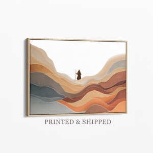 Könnte beinhalten: Abstrakter Kunstdruck mit einer Figur mit Stab, die durch eine geschichtete Landschaft in warmen Erdtönen geht. Das Kunstwerk ist in einem goldfarbenen Rahmen eingefasst, was eine minimalistische und ruhige Ästhetik schafft. Der Text "PRINTED & SHIPPED" befindet sich unten.