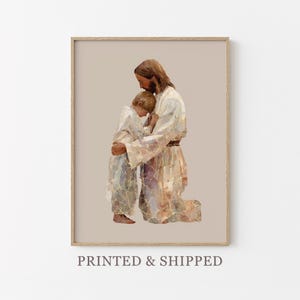 May include: Framed art print showing a figure in a white robe embracing a child. The artwork uses warm tones of beige, brown, and gold, with a textured, mosaic-like effect. The text "PRINTED & SHIPPED" is at the bottom of the frame.