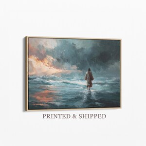 以下が含まれることがあります： 水面を歩く人物を描いた額入りのアートプリント。青、オレンジ、グレーの色合いのドラマチックな空を背景にしています。アートワークは明るい色の木製フレームに収められています。「PRINTED & SHIPPED」の文字がフレームの下部に印刷されています。