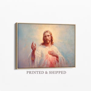 Puede incluir: Una impresión de arte mural enmarcada que presenta una pintura de Jesucristo con cabello castaño largo y barba, vistiendo una túnica blanca. Una suave luz dorada irradia detrás de la cabeza y un resplandor rojo emana del área del pecho.