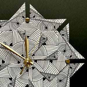 May include: A wall clock featuring a star-shaped face with a black and white geometric pattern of concentric arcs. The clock has three gold-colored metal hands and small gold-colored circular fasteners at the points of the star-shaped design.