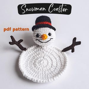 May include: A handmade crochet snowman coaster. The coaster is white with a black top hat, orange nose, and brown stick arms. The text "Snowman Coaster" is above the snowman, and "pdf pattern" is to the left.