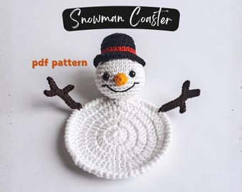 Könnte beinhalten: Ein gehäkelter Schneemann-Untersetzer. Der Untersetzer ist weiß mit einem schwarzen Zylinder, einer orangenen Nase und braunen Astarmen. Der Text "Snowman Coaster" steht darüber, und "pdf pattern" links.