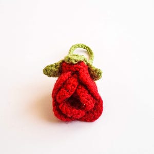 May include: A handmade crochet rose in vibrant red, with green leaves and a loop. The flower is detailed with textured stitches, showcasing a handcrafted aesthetic. This decorative item is perfect for adding a touch of nature-inspired charm.