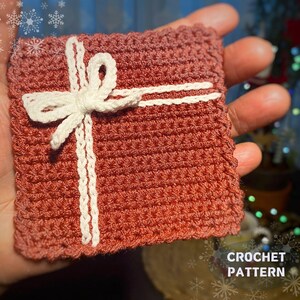 May include: A crocheted gift box with a white bow. The box is made with a red yarn and has a white crocheted ribbon.