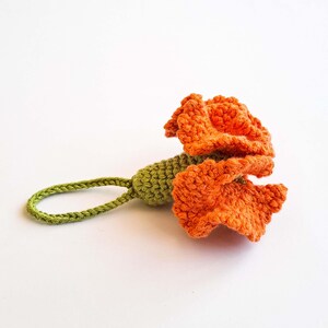 May include: A handmade crochet flower in vibrant orange, with a green stem and loop. The flower's petals are textured, and the loop is designed for hanging. This decorative item is perfect for adding a touch of handmade charm.