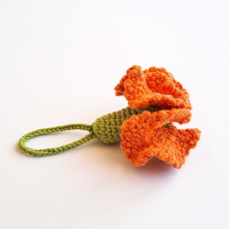 May include: A handmade crochet flower in vibrant orange, with a green stem and loop. The flower's petals are textured, and the loop is designed for hanging. This decorative item is perfect for adding a touch of handmade charm.