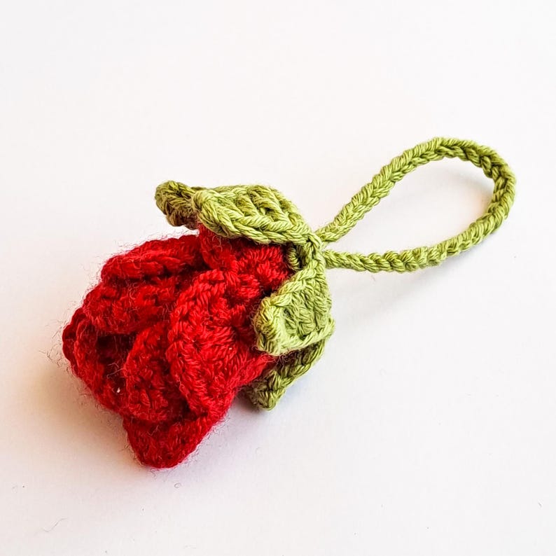 Crochet rose keychain with layered red petals and green leaf base – handmade flower design.