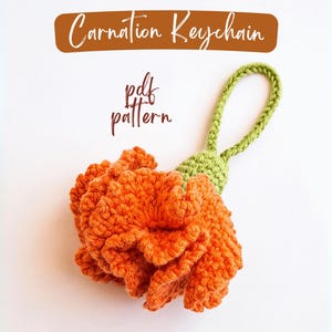 Peut inclure: Un porte-clés en forme d'œillet orange crocheté, avec une tige et une boucle vertes. Le porte-clés est fait à la main et présente un motif floral détaillé. Le texte sur l'image indique "Carnation Keychain" et "pdf pattern".