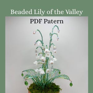 Puede incluir: Una planta de lirio de los valles con cuentas en una maceta de terracota. La planta presenta cuentas de flores blancas, tallos de cuentas verdes y un lecho de musgo verde. El texto "Beaded Lily of the Valley PDF Pattern" está en la parte superior.