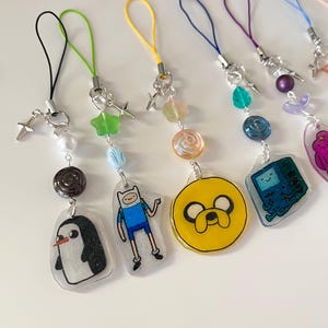 以下が含まれることがあります： アニメシリーズ「アドベンチャータイム」のキャラクターをフィーチャーした、カラフルな携帯電話用チャーム7個セット。チャームには、フィン・ザ・ヒューマン、ジェイク・ザ・ドッグ、BMOなどが含まれています。各チャームは、キラキラとした仕上げのクリアレジン製で、小さなビーズと星型のチャームが付いています。
