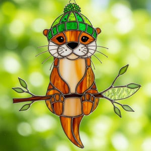 Pode incluir: Vitral de uma lontra com tons laranja e castanho, usando um chapéu verde, pousada num galho com folhas verdes. A obra de arte tem um rosto branco, olhos pretos e um fundo verde desfocado.