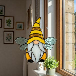May include: A stained glass gnome with a yellow and black striped hat, white beard, and blue-green wings. The gnome is suspended from a chain in front of a window. The gnome's body is yellow and orange.
