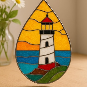 Puede incluir: Vidriera de un faro en forma de lágrima. El faro es blanco con tejado rojo, ribetes negros, y se asienta sobre una base verde y marrón. El fondo muestra un cielo amarillo y agua azul.