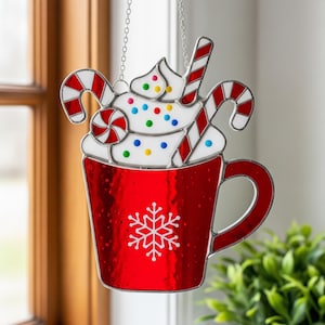 Könnte beinhalten: Rote Glasmalerei-Dekoration in Form einer heißen Schokoladen-Tasse, mit Schlagsahne und Zuckerstangen. Die Tasse hat ein weißes Schneeflocken-Design. Sie hängt an einer silbernen Kette. Maße in Zentimetern.