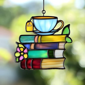 May include: Stained glass suncatcher featuring a stack of books topped with a teacup and tea bag. The books are in various colors, including green, yellow, purple, and red. The teacup is light blue with a gold rim. A decorative butterfly and leaf are also included.
