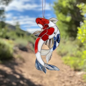 Peut inclure: Deux poissons koï en verre teinté, l'un rouge et blanc, l'autre bleu et blanc, sont entrelacés dans un motif décoratif.