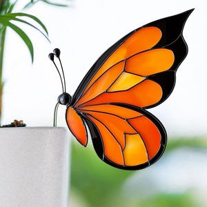 May include: Orange and black stained glass butterfly decoration. The butterfly is perched on the edge of a white planter.