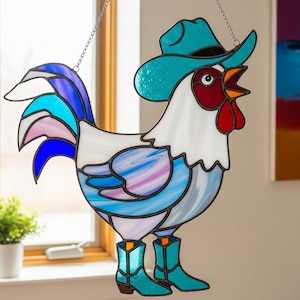 Puede incluir: Gallo de vidriera con sombrero y botas de vaquero turquesa. El gallo tiene un cuerpo blanco con detalles azules, morados y rosas. La cresta y la barba del gallo son rojas. Una pieza decorativa para una ventana.