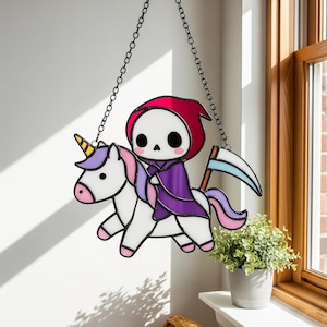 May include: A stained glass window hanging featuring a cartoon Grim Reaper riding a unicorn. The Grim Reaper wears a purple cloak and a red hood. The unicorn is white with a purple mane and tail. A black chain suspends the window.
