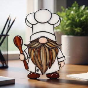 May include: Stained glass chef gnome figurine. The gnome wears a white chef's hat and coat, holding a wooden spoon. The beard is a mix of brown and tan glass. The figurine is on a wooden surface.