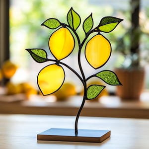 Puede incluir: Una escultura de árbol de limón de vidrio emplomado con tres limones amarillos y hojas verdes. La escultura está montada sobre una base de madera negra.