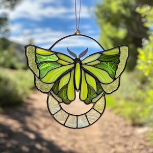 May include: A stained glass butterfly suncatcher with green and yellow wings. The butterfly is hanging from a circular frame with a clear background.