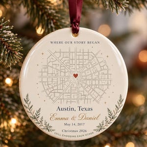 May include: A round white ceramic ornament hanging from a dark red ribbon. The front features a black street map with a red heart, the text WHERE OUR STORY BEGAN, Austin, Texas, Emma & Daniel, May 14, 2017, Christmas 2026, and STILL CHOOSING EACH OTHER.